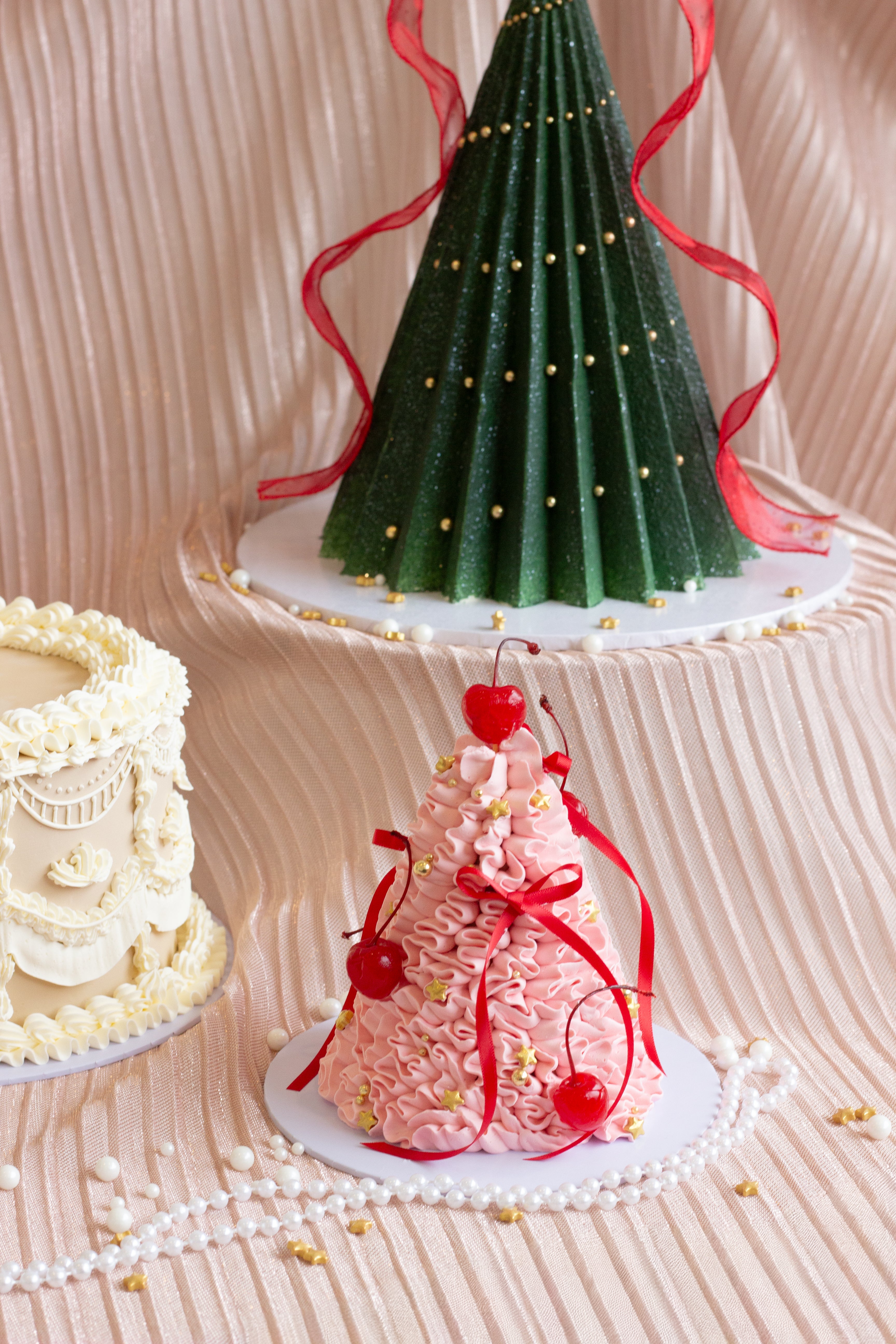 Pink Christmas tree shaped cake with expressive buttercream piping, red ribbons, and cherries on top.