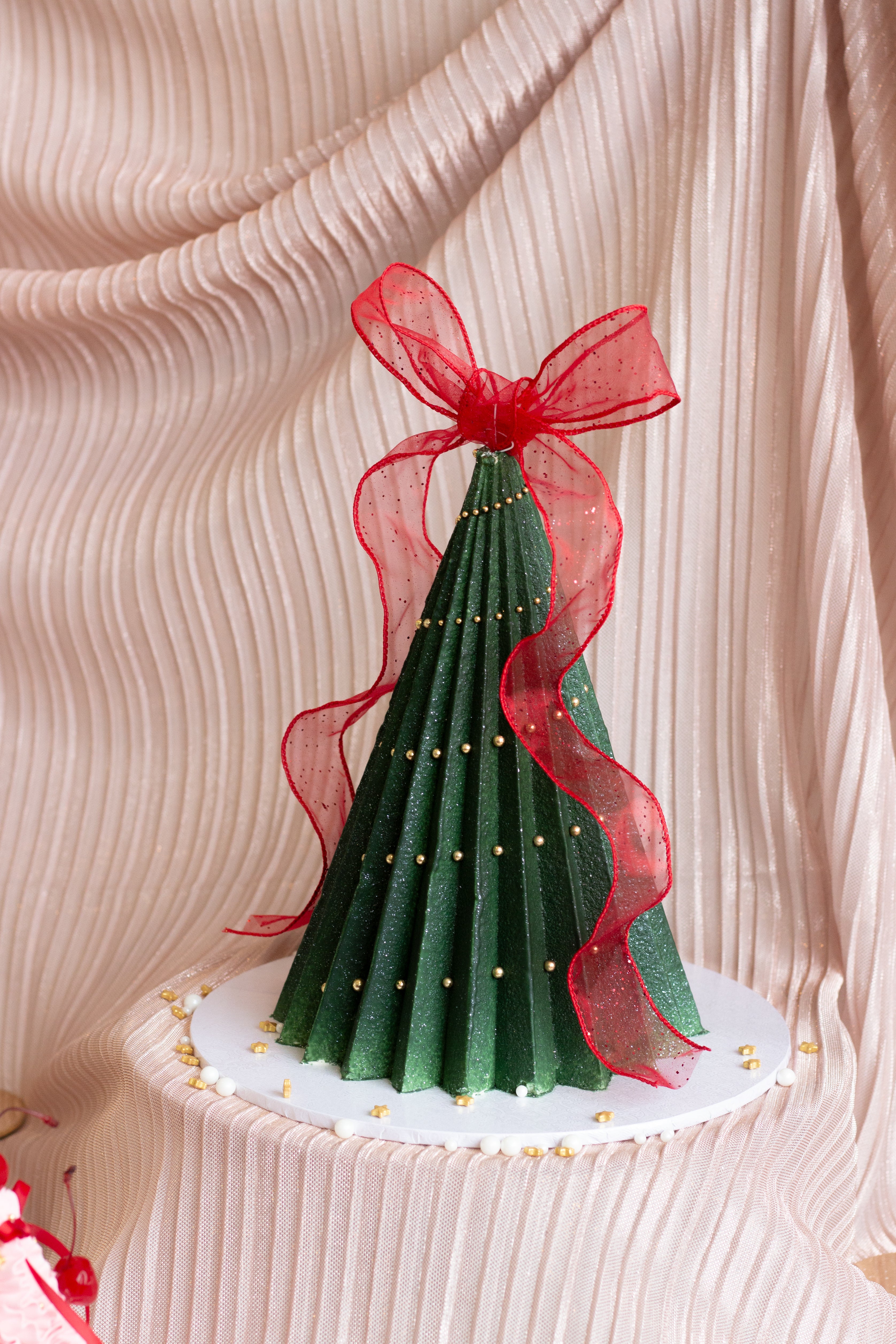 A handcrafted Christmas tree cake featuring deep green buttercream ruffles, delicate ribbon details, and a festive sculpted design. Perfect for holiday tables and gift giving in Melbourne and beyond. Cake Melbourne. Christmas cake Melbourne.