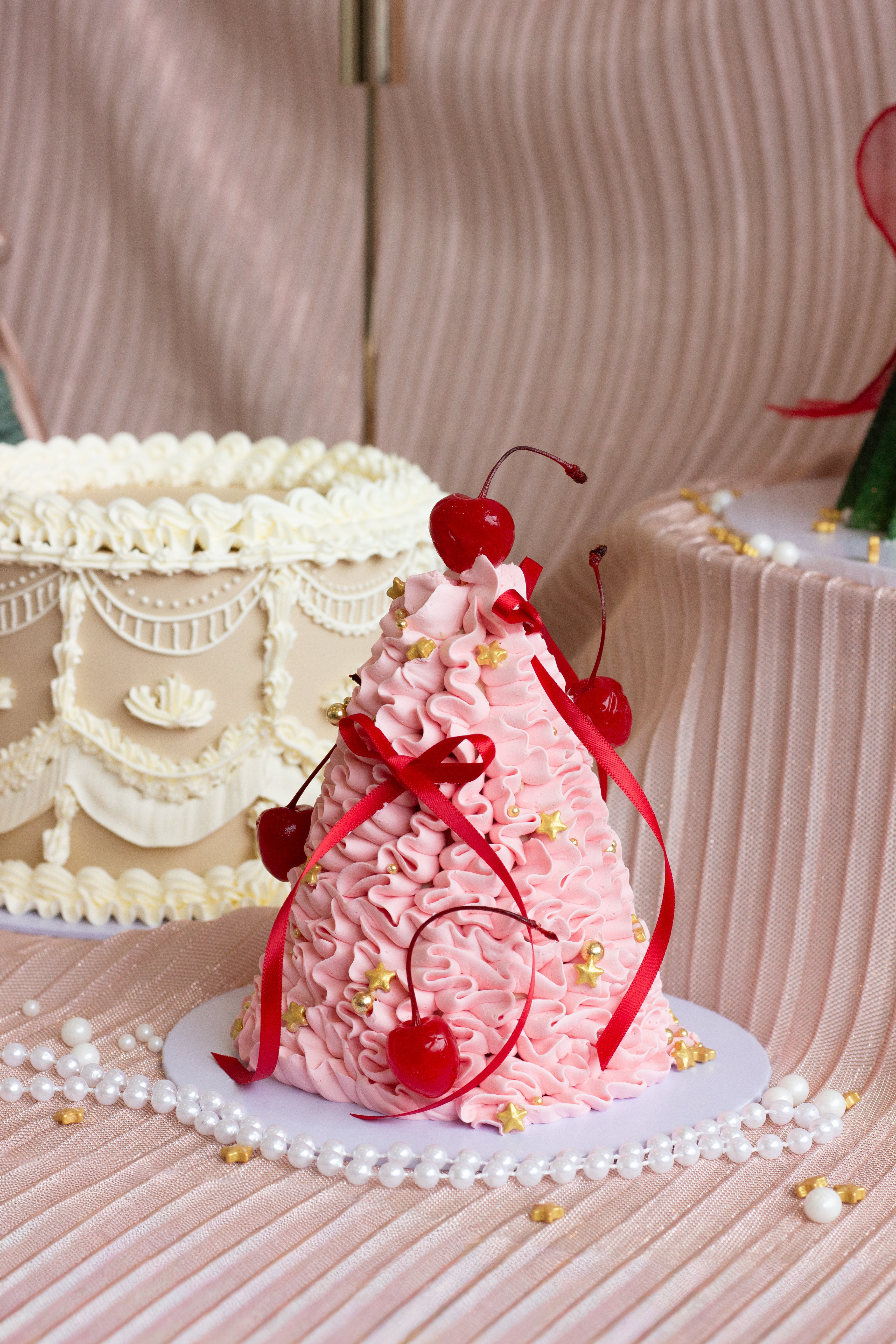 Pink Christmas tree shaped cake with expressive buttercream piping, red ribbons, and cherries on top.