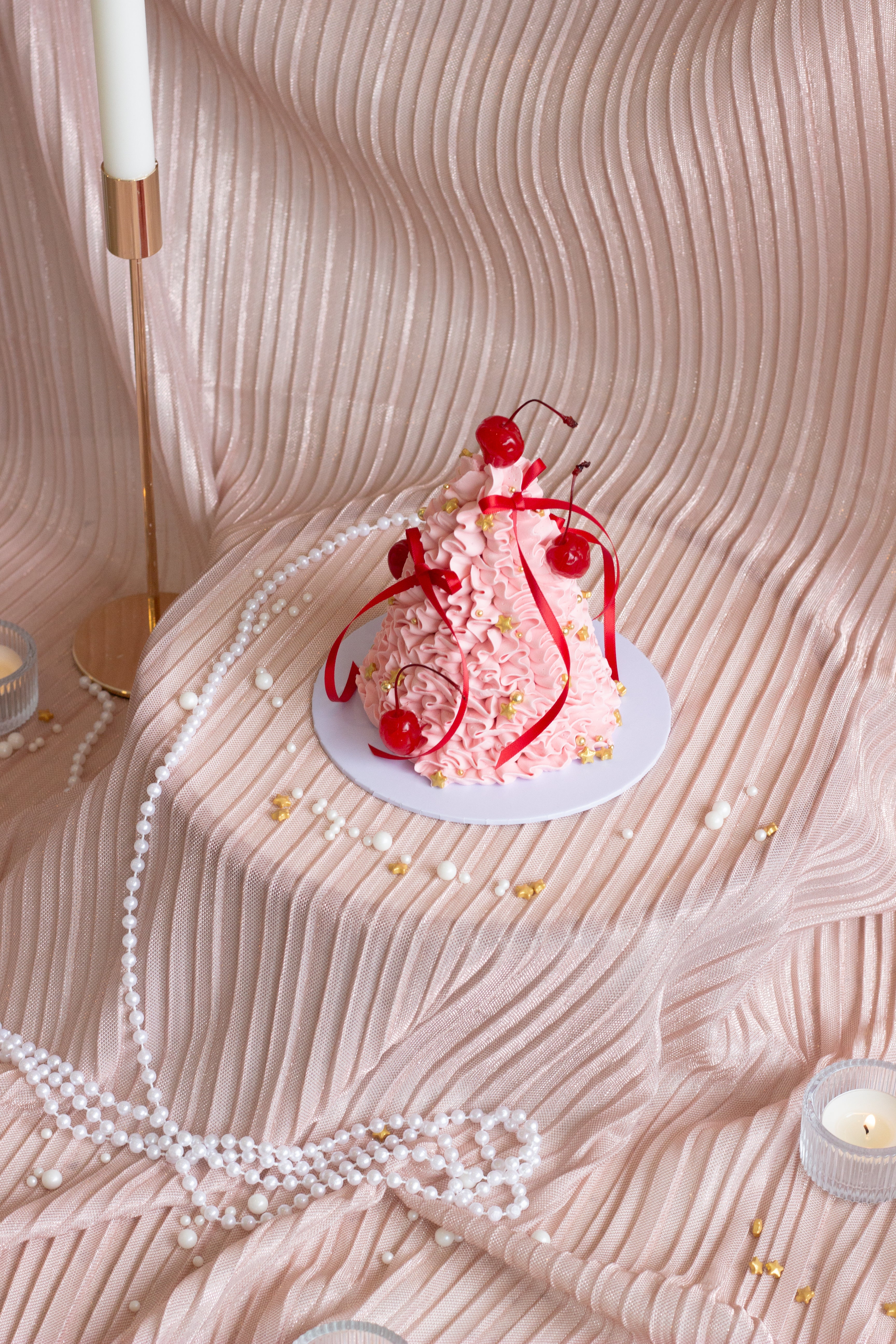 Pink Christmas tree shaped cake with expressive buttercream piping, red ribbons, and cherries on top.